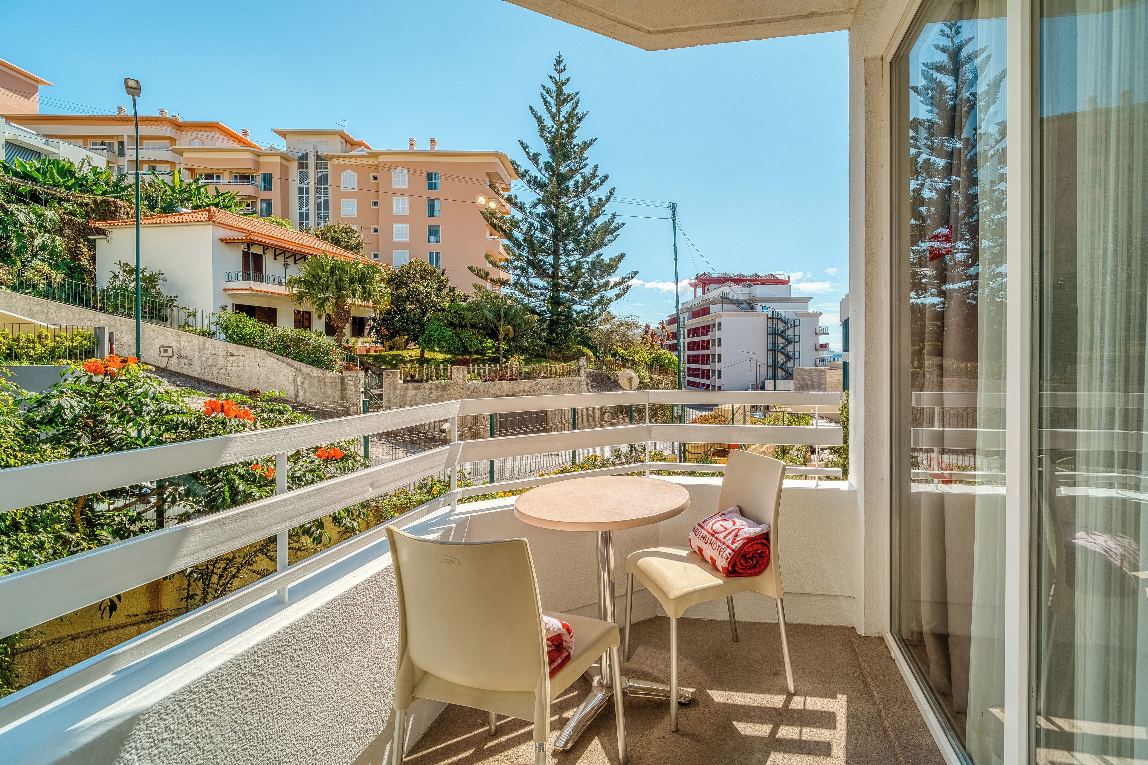 Un balcón con mesa y sillas, con vista a un jardín y edificios.