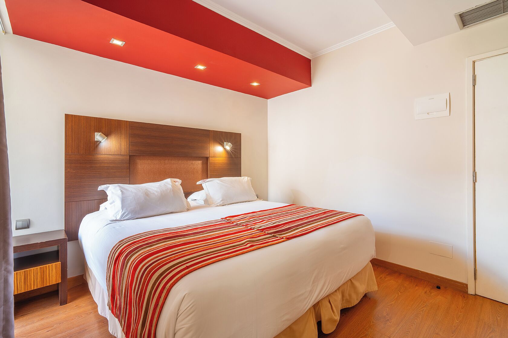 Una habitación de hotel con una cama, cabecero de madera, techo rojo y una puerta.