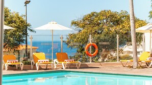 Zona junto a la piscina con sillones de descanso, sombrillas y un flotador.