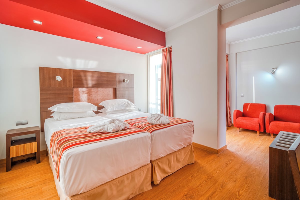 A hotel room with a large bed, a wooden nightstand, a red accent wall, and two red armchairs.