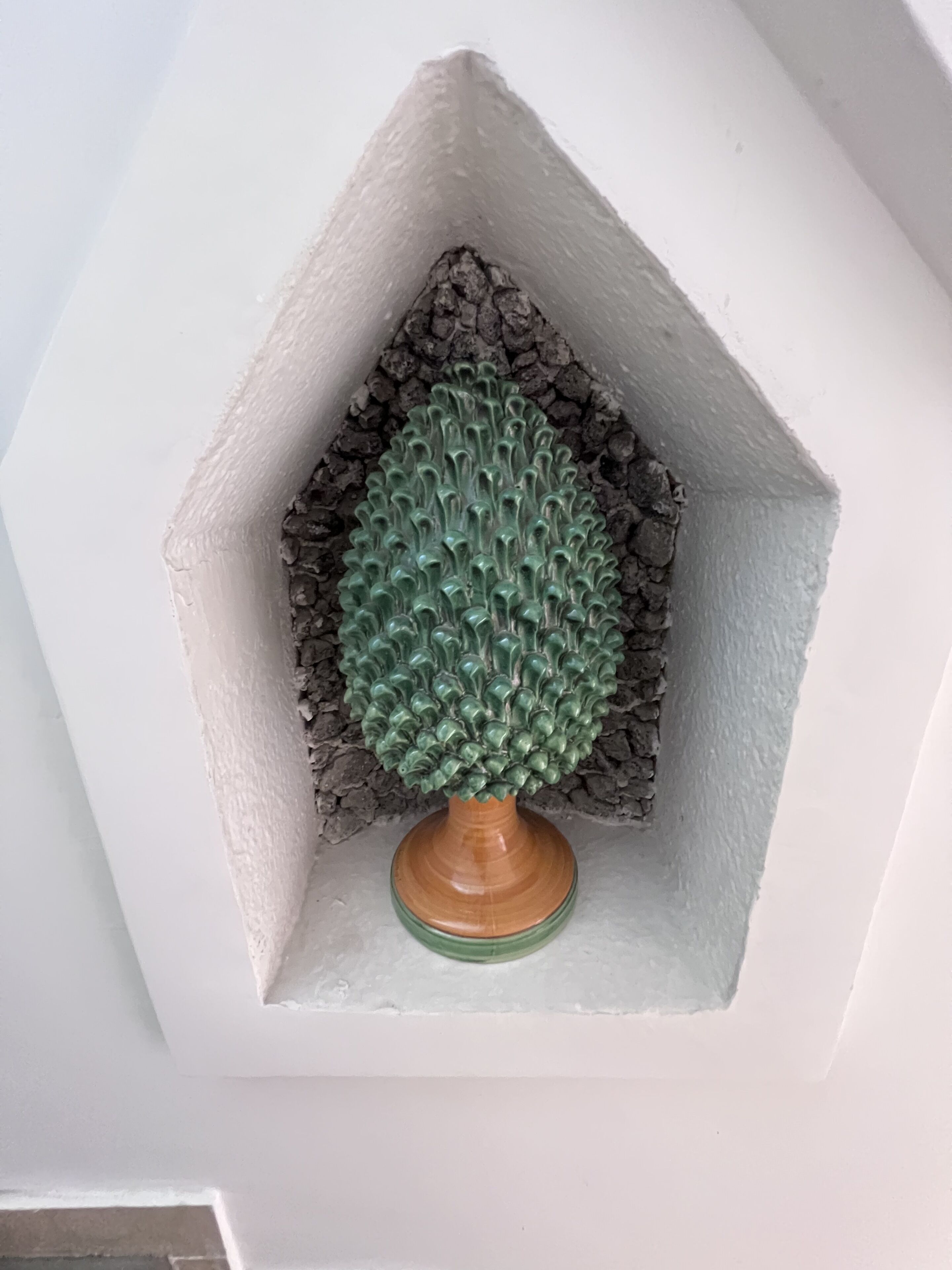 A corner of a room with a white wall and a green textured object resembling a tree in a corner.
