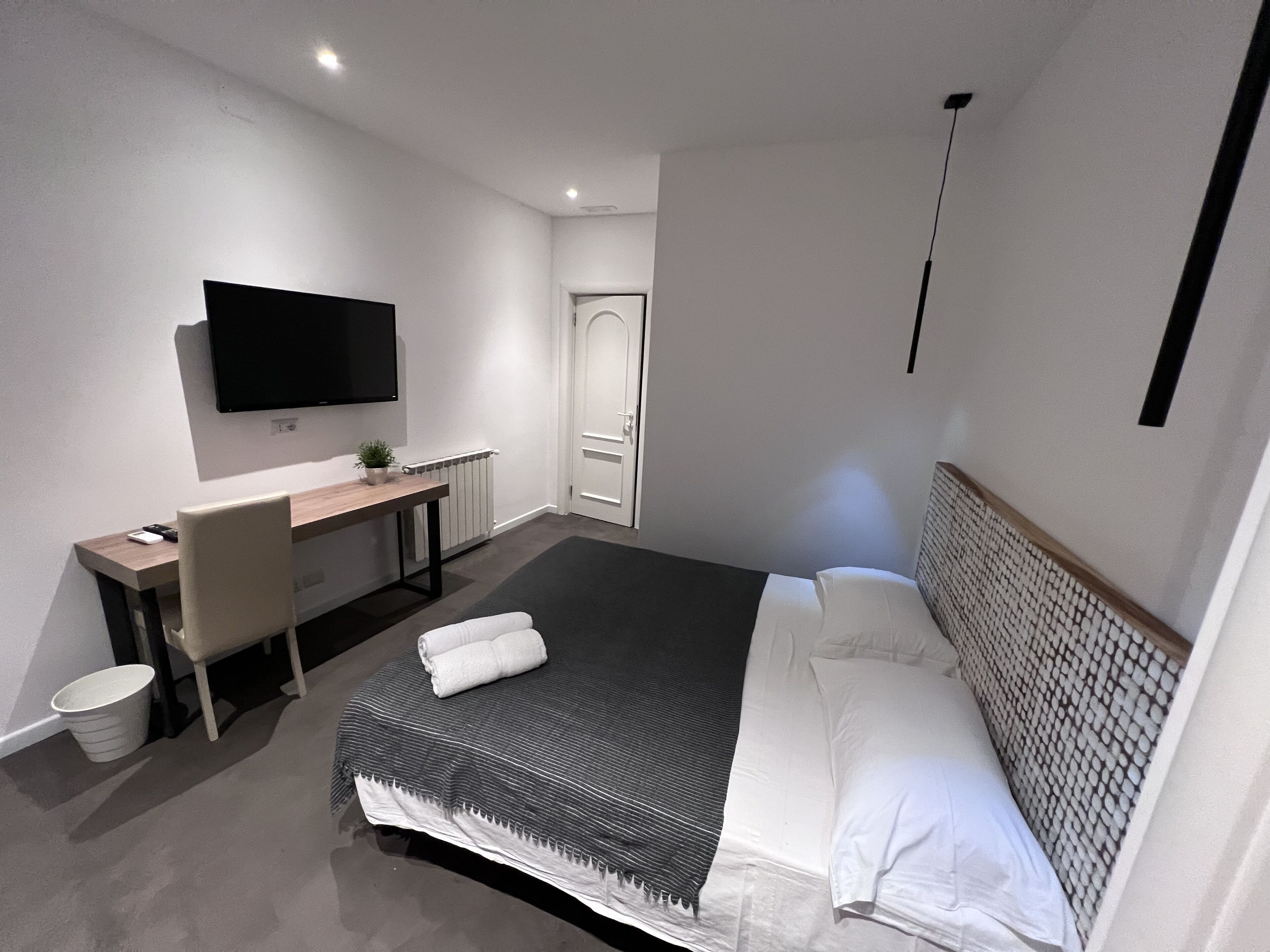 Una camera d'albergo moderna con un letto grande, una scrivania, una sedia, una televisione e un termosifone.