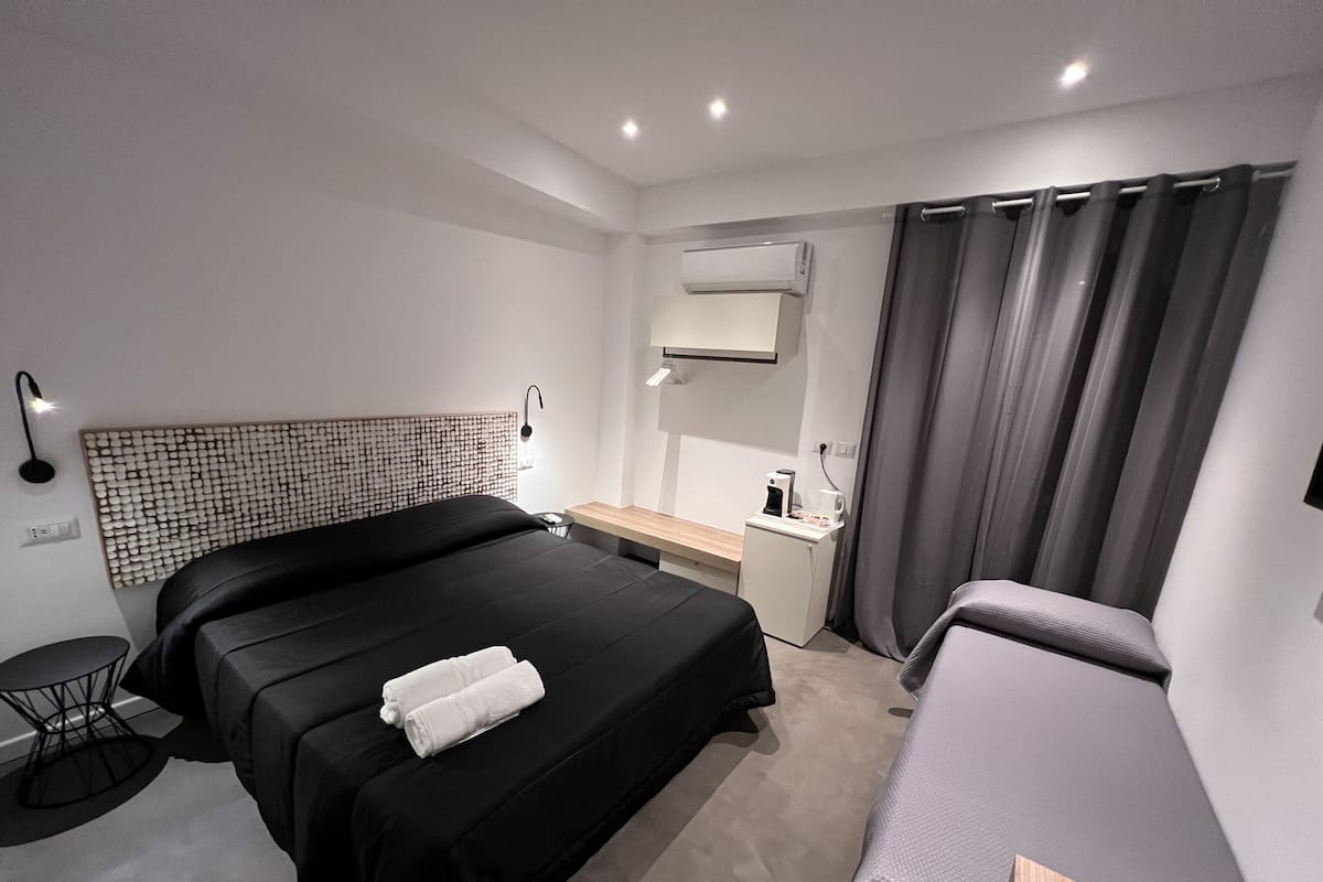 Moderni hotellihuone, jossa on suuri sänky, työpöytä, pieni jääkaappi ja yöpöytä.