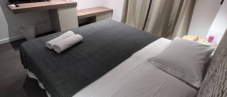 Una habitación de hotel moderna con cama, escritorio, televisor de pantalla plana, una planta pequeña y ventana con cortinas.