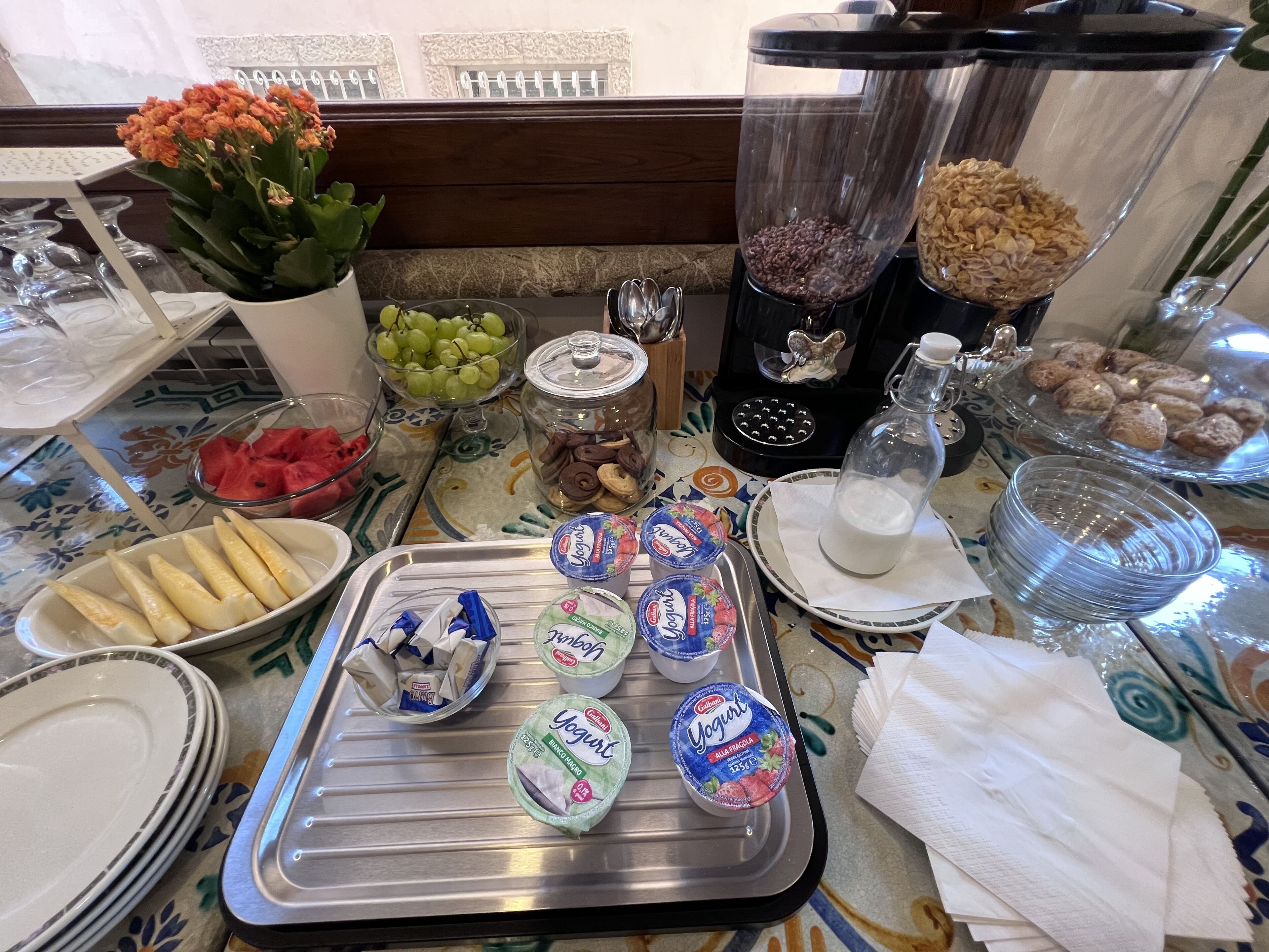 A buffet table with various food items including grapes, watermelon, cookies, and yogurt.