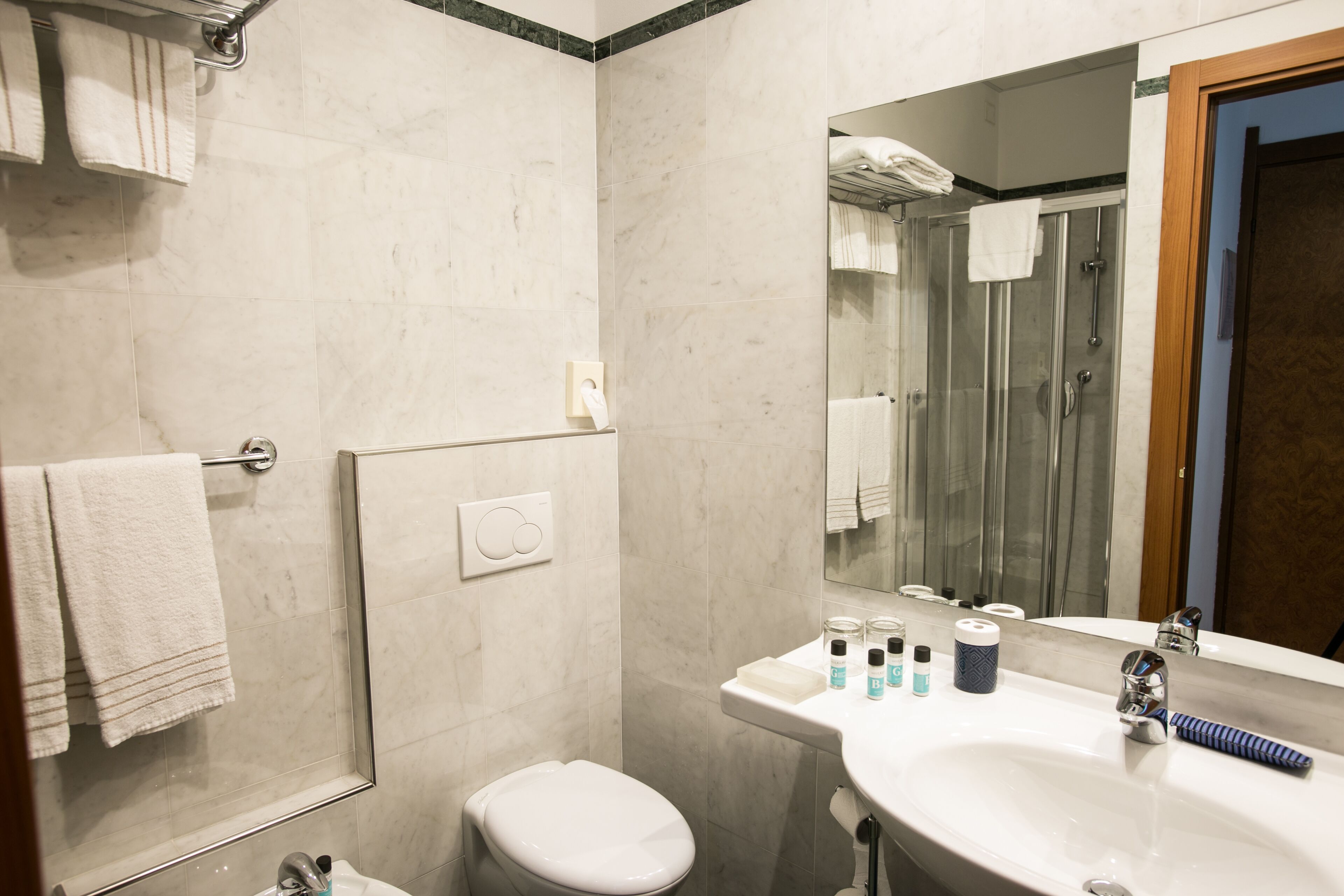 Une salle de bain avec des toilettes, un lavabo et une douche. Des serviettes sont suspendues sur un porte-serviettes, et un miroir est placé au-dessus du lavabo.