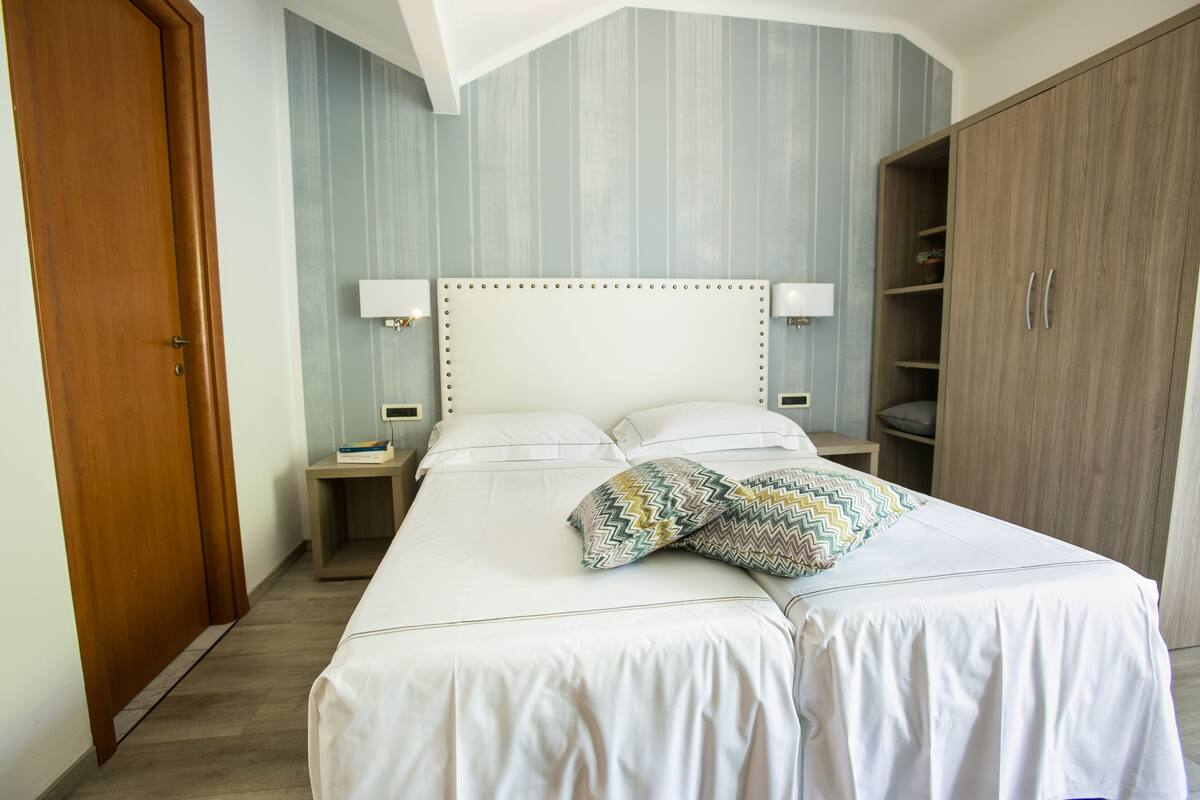 Une chambre d’hôtel avec un grand lit, une armoire, une table de chevet et une lampe.