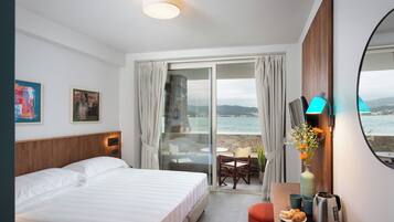 Ein Hotelzimmer mit Bett, Schreibtisch mit Kaffeemaschine, Blumen in einer Vase, Blick aufs Meer und einem Bild an der Wand.