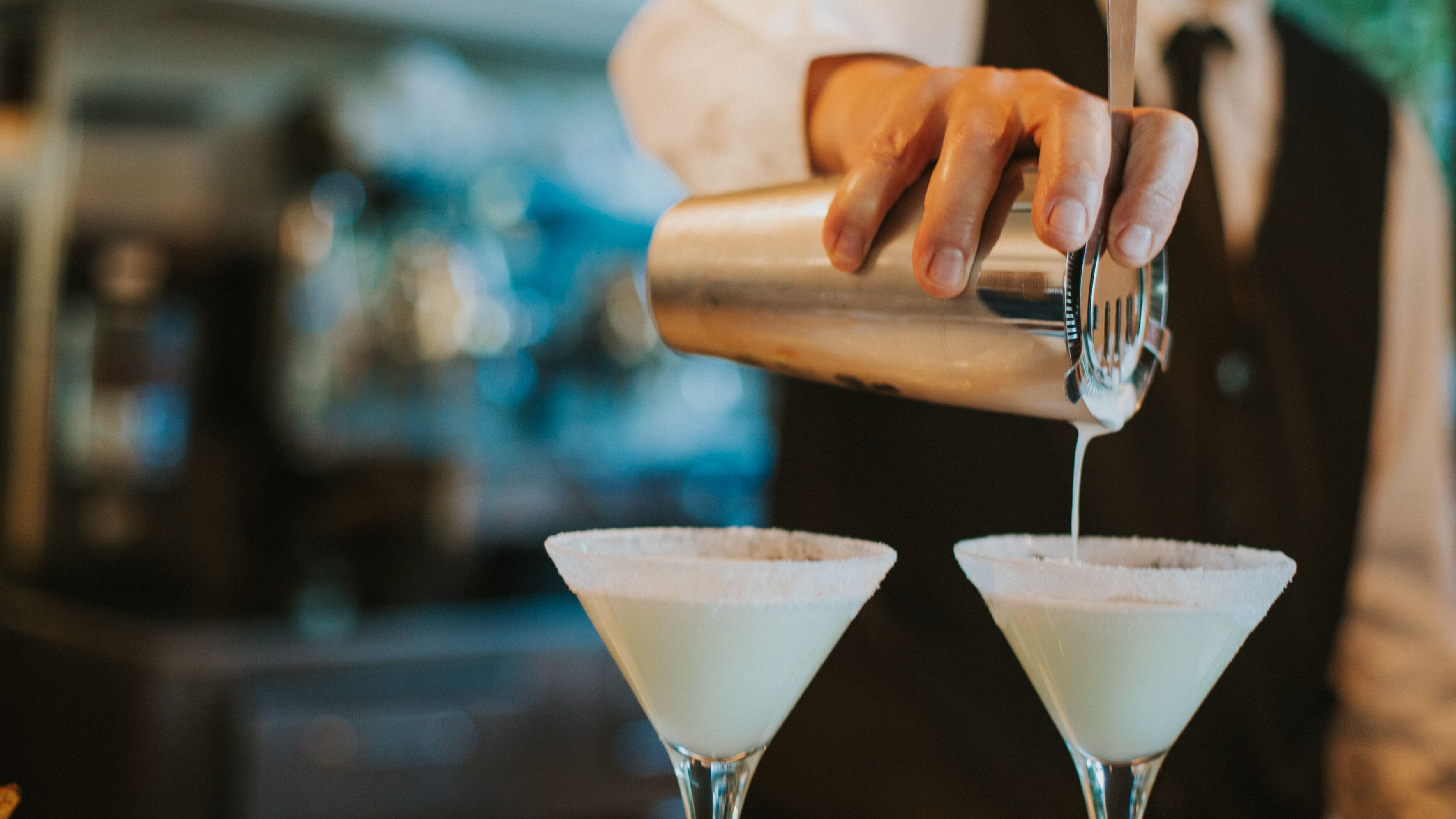 A bartender pouring a drink into a martini glass.
