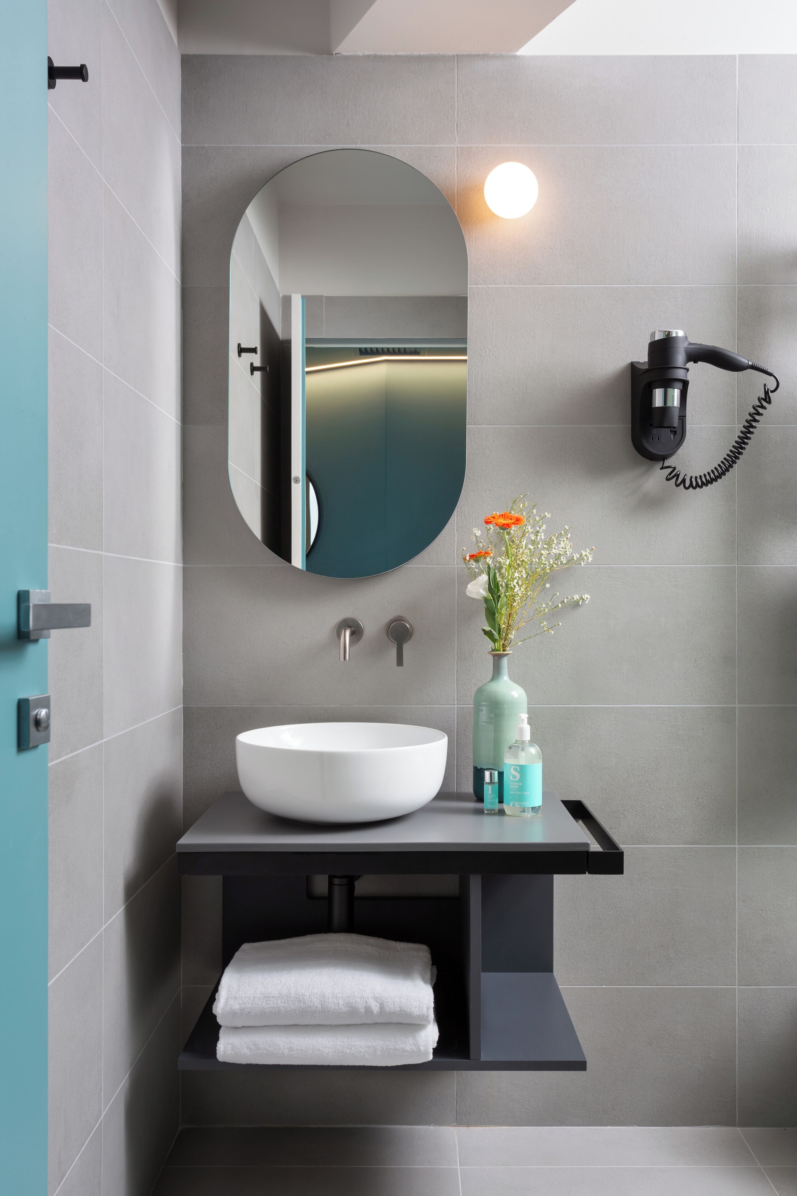 A modern bathroom with a white sink, a mirror, and a hairdryer mounted on the wall.