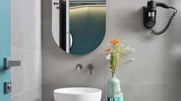 A modern bathroom with a white sink, a mirror, and a hairdryer mounted on the wall.