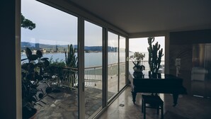 Een ruim balkon met uitzicht op een meer en bergen, met potplanten en een piano.