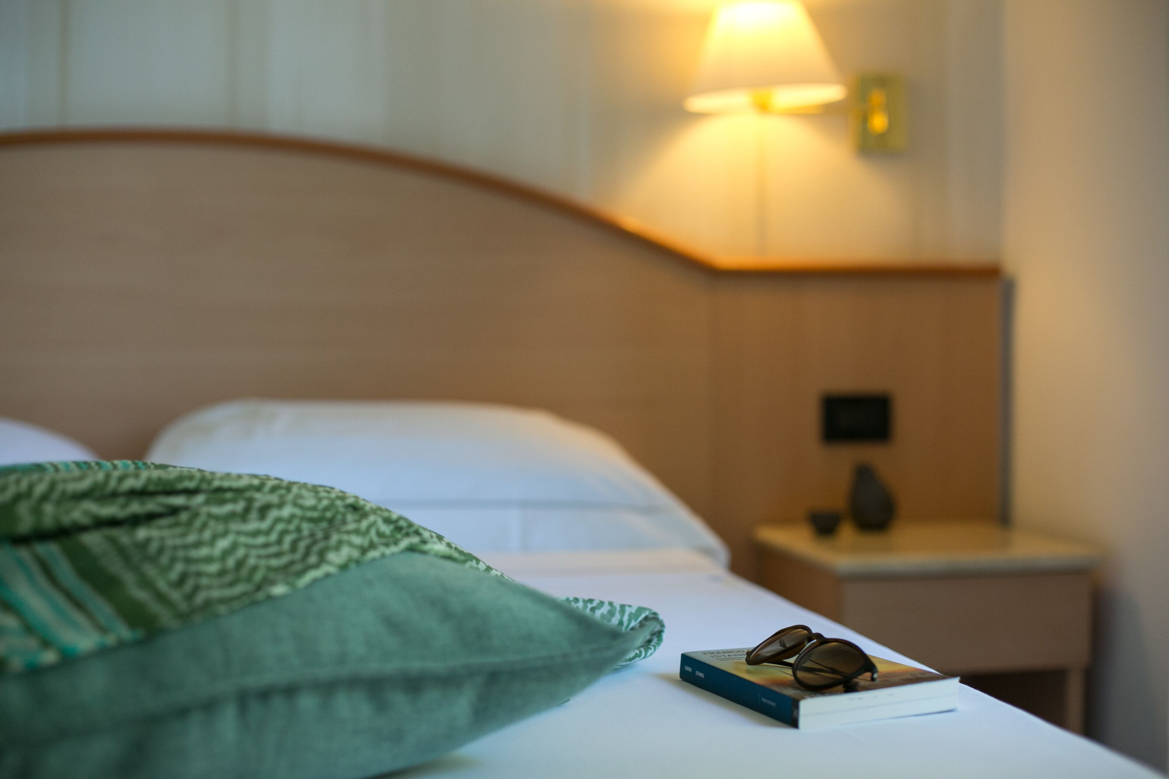 Una cama bien hecha con un edredón verde, un par de gafas y un libro en la mesita de noche.