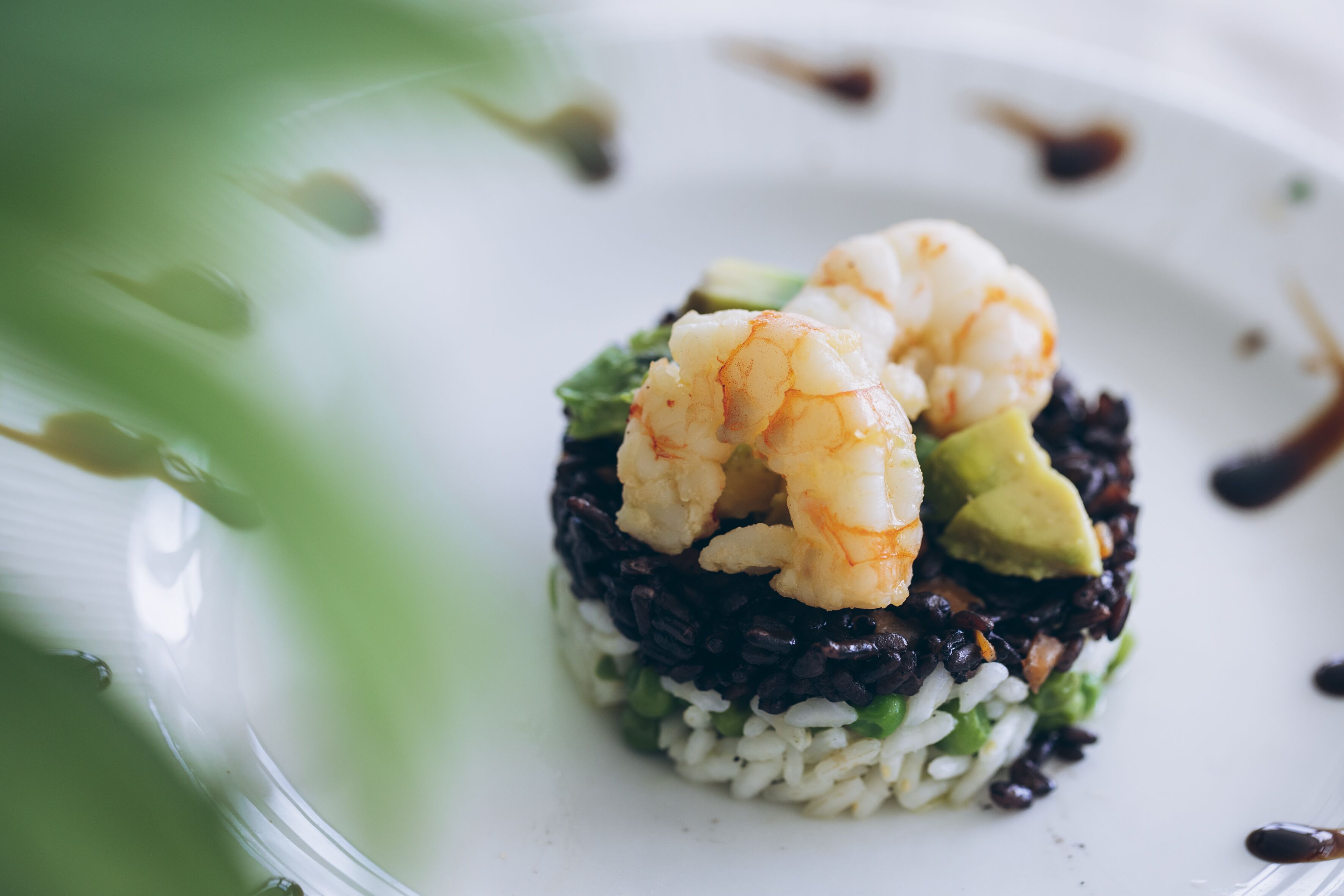 Un plato con un plato de sushi de arroz, arroz negro, aguacate y camarones.