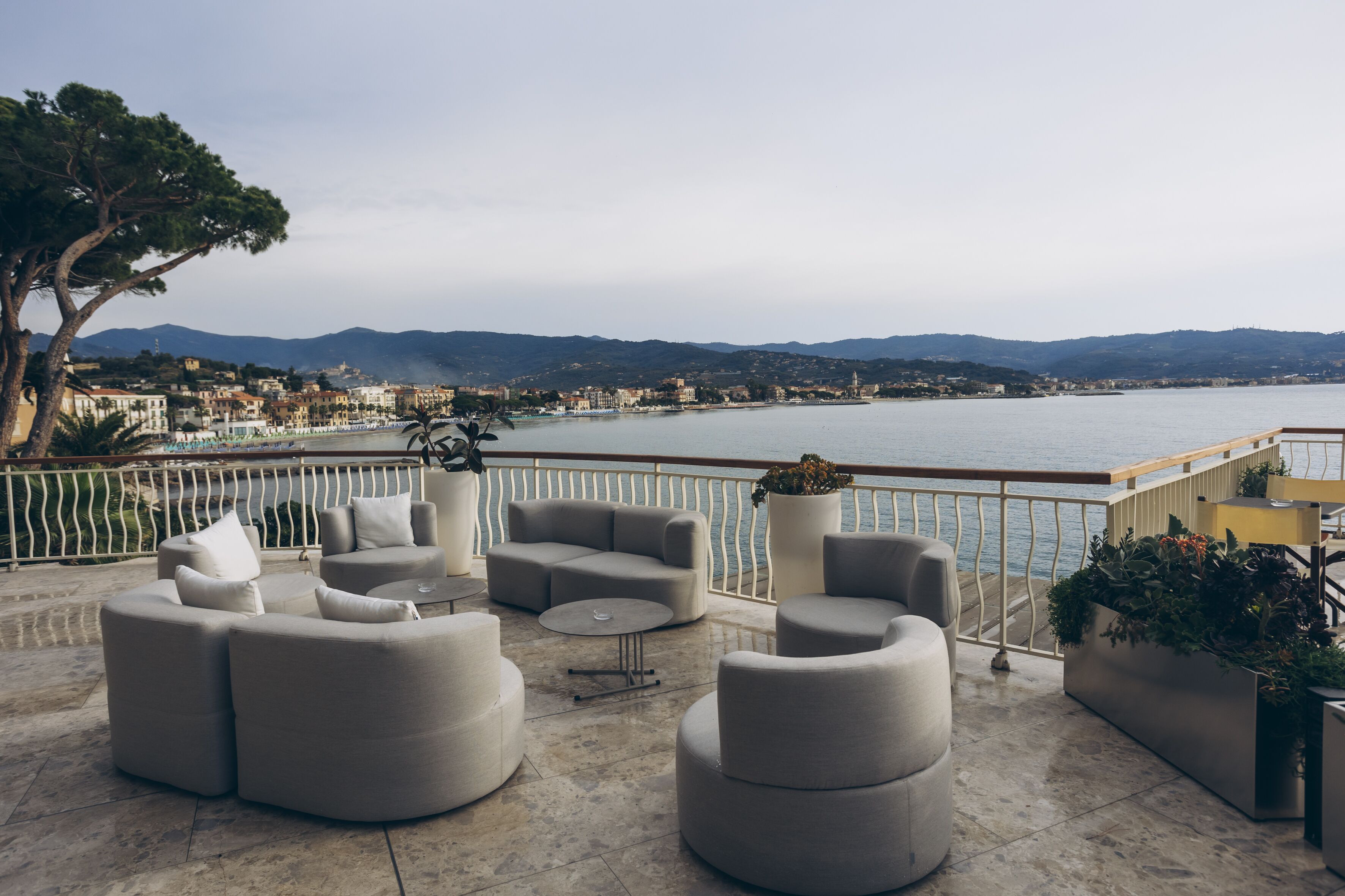Una terraza con muebles modernos, vista al mar y colinas al fondo.