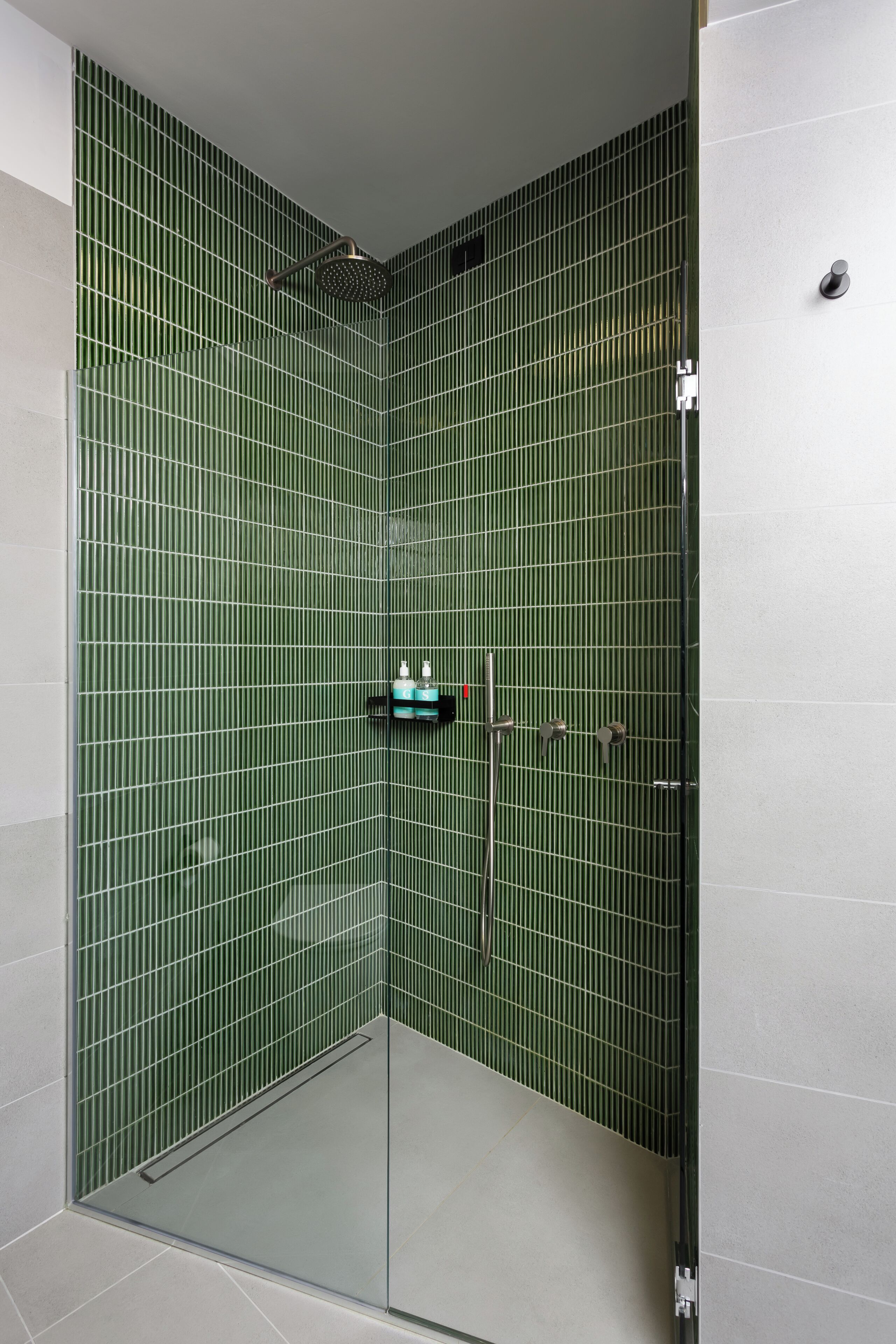 Una ducha con paredes de azulejos verdes y cabezal de ducha metálico, completamente cerrada por un cristal.
