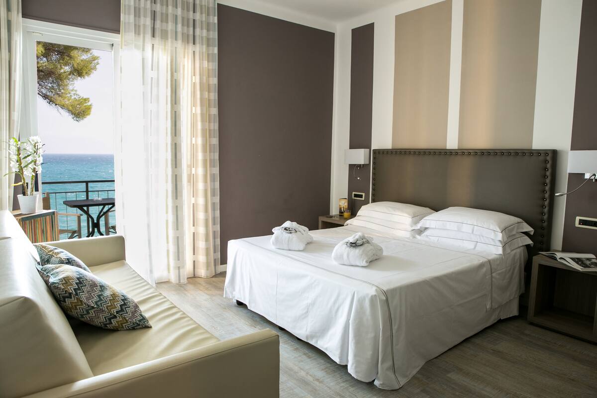 Une chambre d’hôtel avec un grand lit, un canapé, une table de chevet et une vue sur la mer.