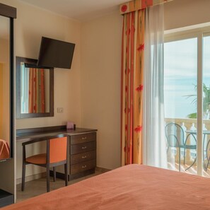 A hotel room with a bed, a desk with a chair, a television, and a balcony with outdoor furniture. - San Vincenzo (Letojanni)