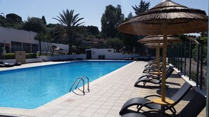 A swimming pool with lounge chairs and umbrellas, surrounded by a tiled deck and greenery. - Calanica Residence Hotel (Cefalù)