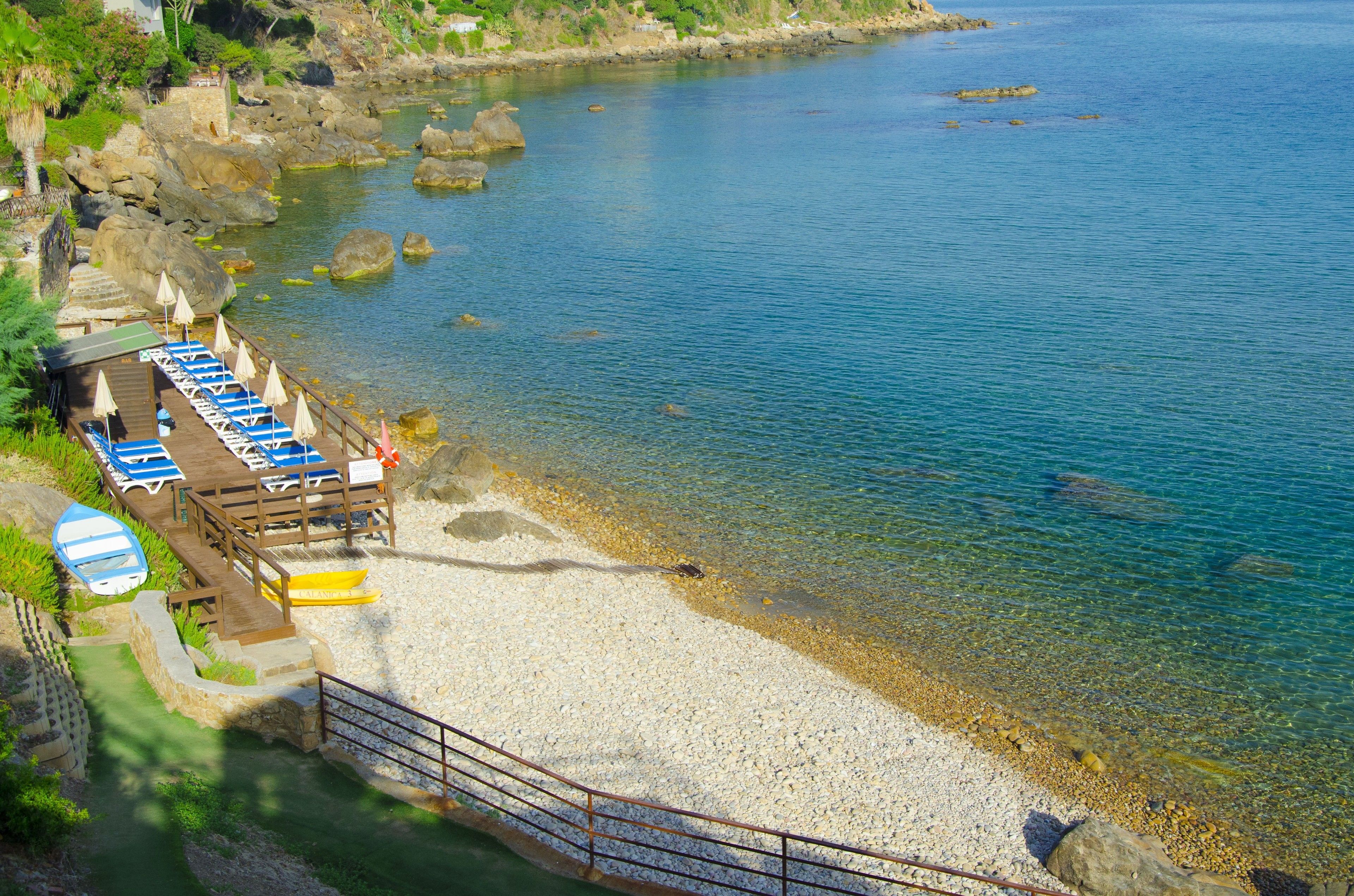 A beachside hotel with a wooden deck, sun loungers, and a clear view of the calm sea.