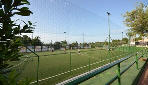 A sports field with a netted enclosure, surrounded by trees and advertising banners. - Calanica Residence Hotel (Cefalù)