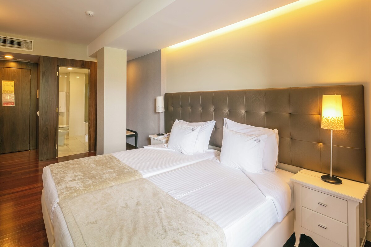 Quarto de hotel com uma cama grande, mesas de cabeceira, um abajur e um espelho.