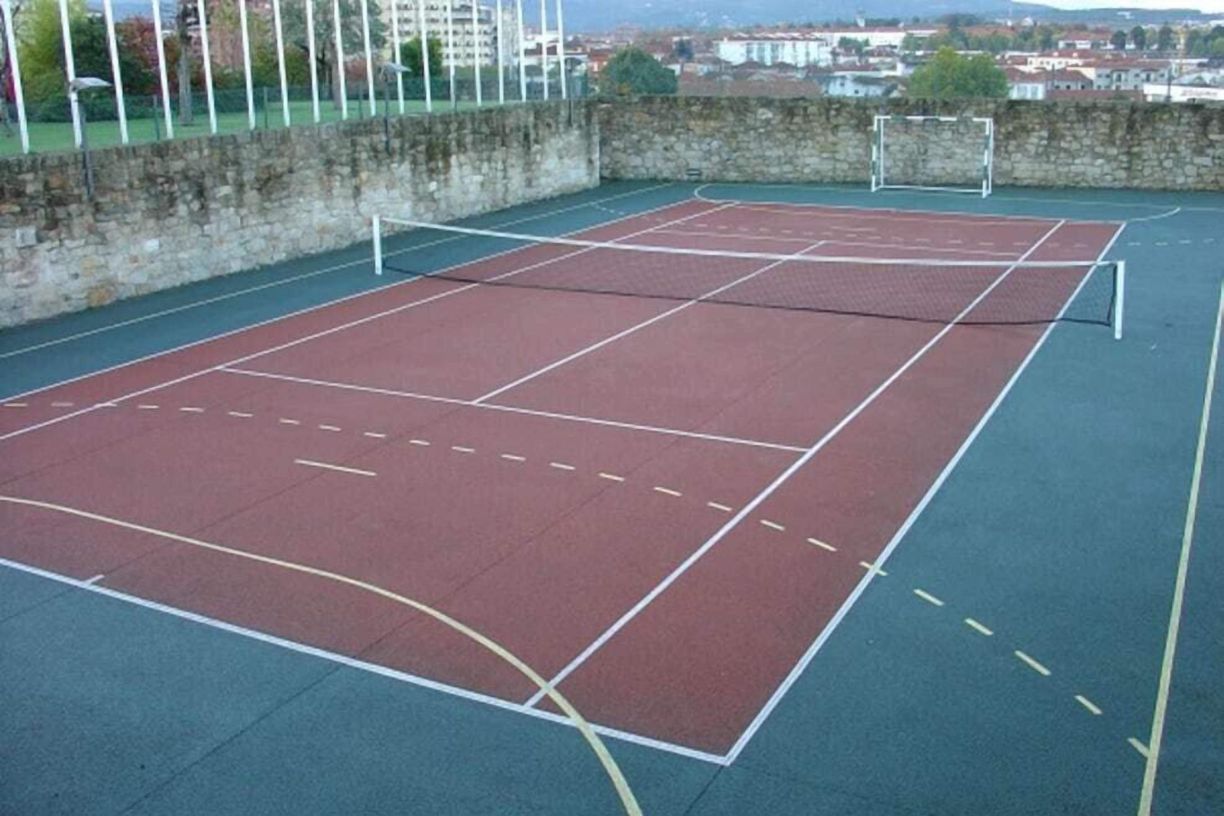 An outdoor tennis court with a net, surrounded by a stone wall and a metal fence.