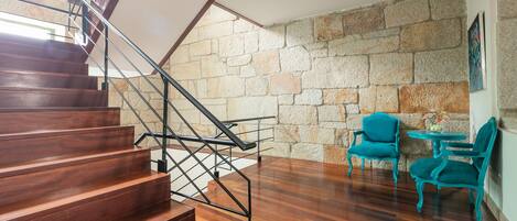 A staircase with wooden steps and metal railings, leading to a room with a stone wall and teal chairs.