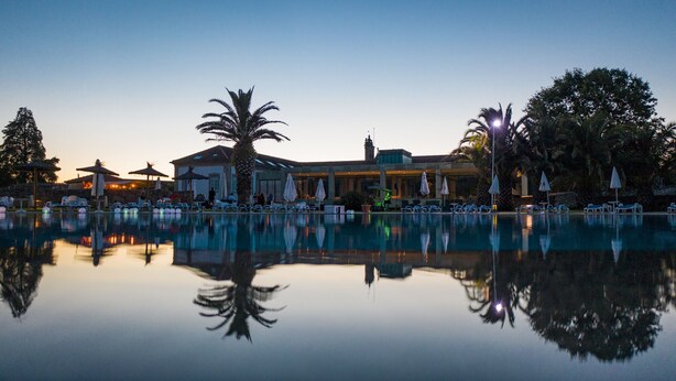 A resort with a large pool, palm trees, and a building with a tiled roof.