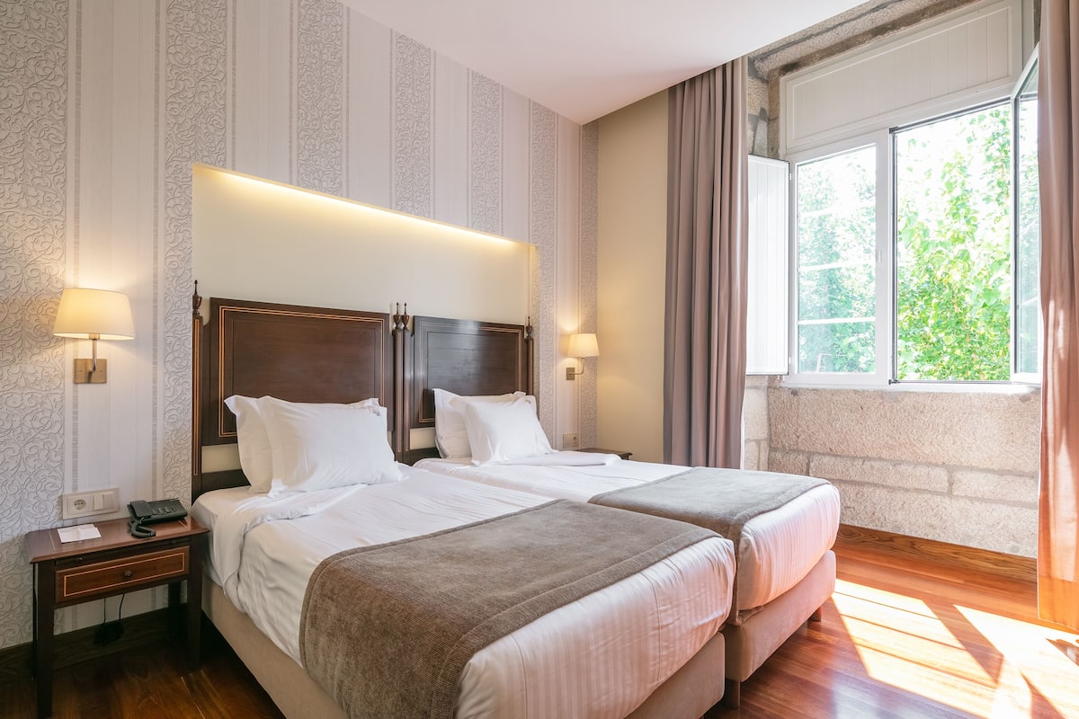 Une chambre d’hôtel avec deux lits, une table de chevet avec un téléphone et une fenêtre avec des rideaux.