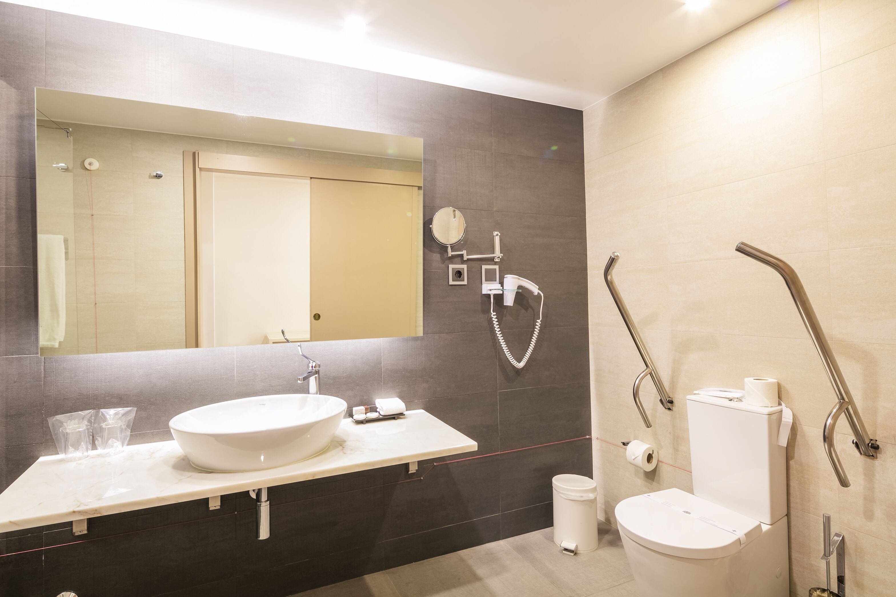 Un baño moderno con un espejo grande, un lavabo y un inodoro.