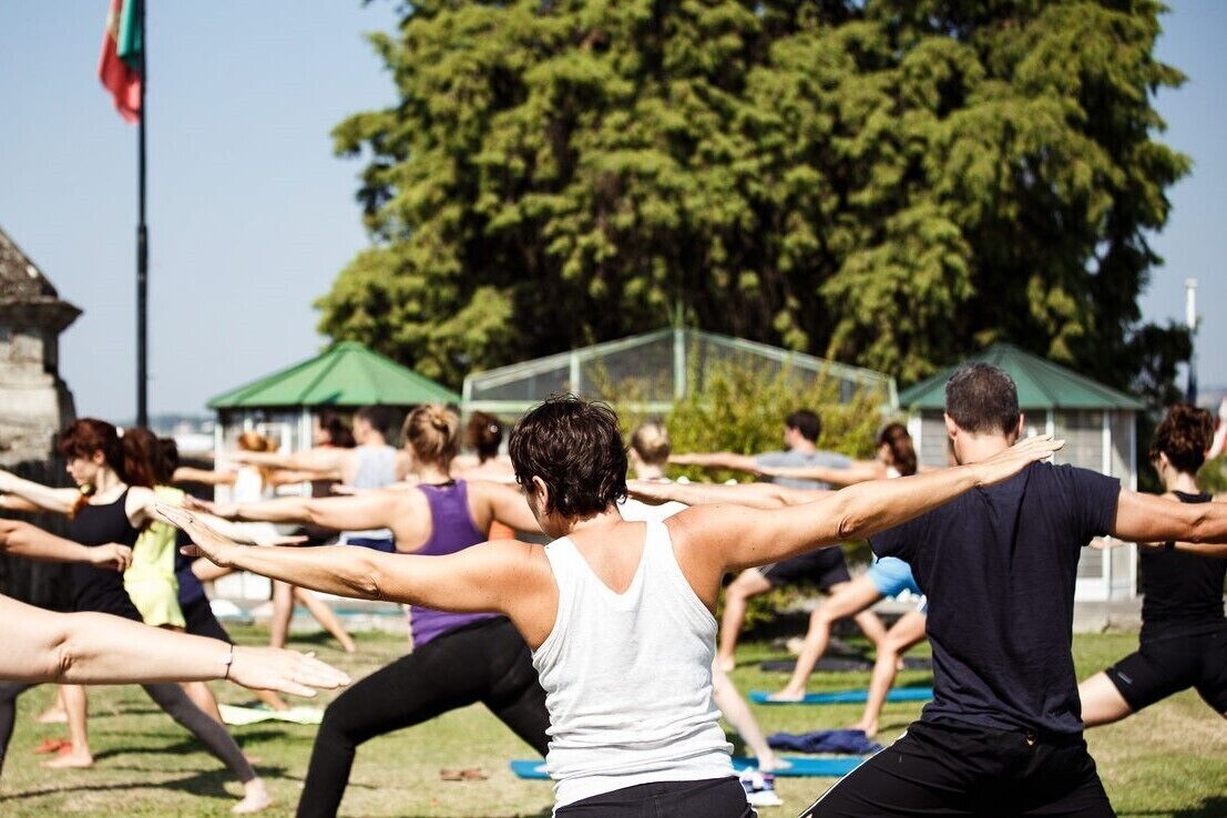 A group of people stretching outdoors in a grassy area with trees and a clear sky.