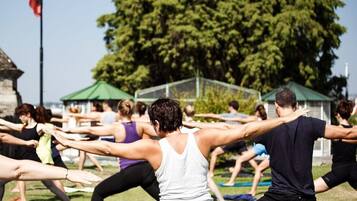 A group of people stretching outdoors in a grassy area with trees and a clear sky.