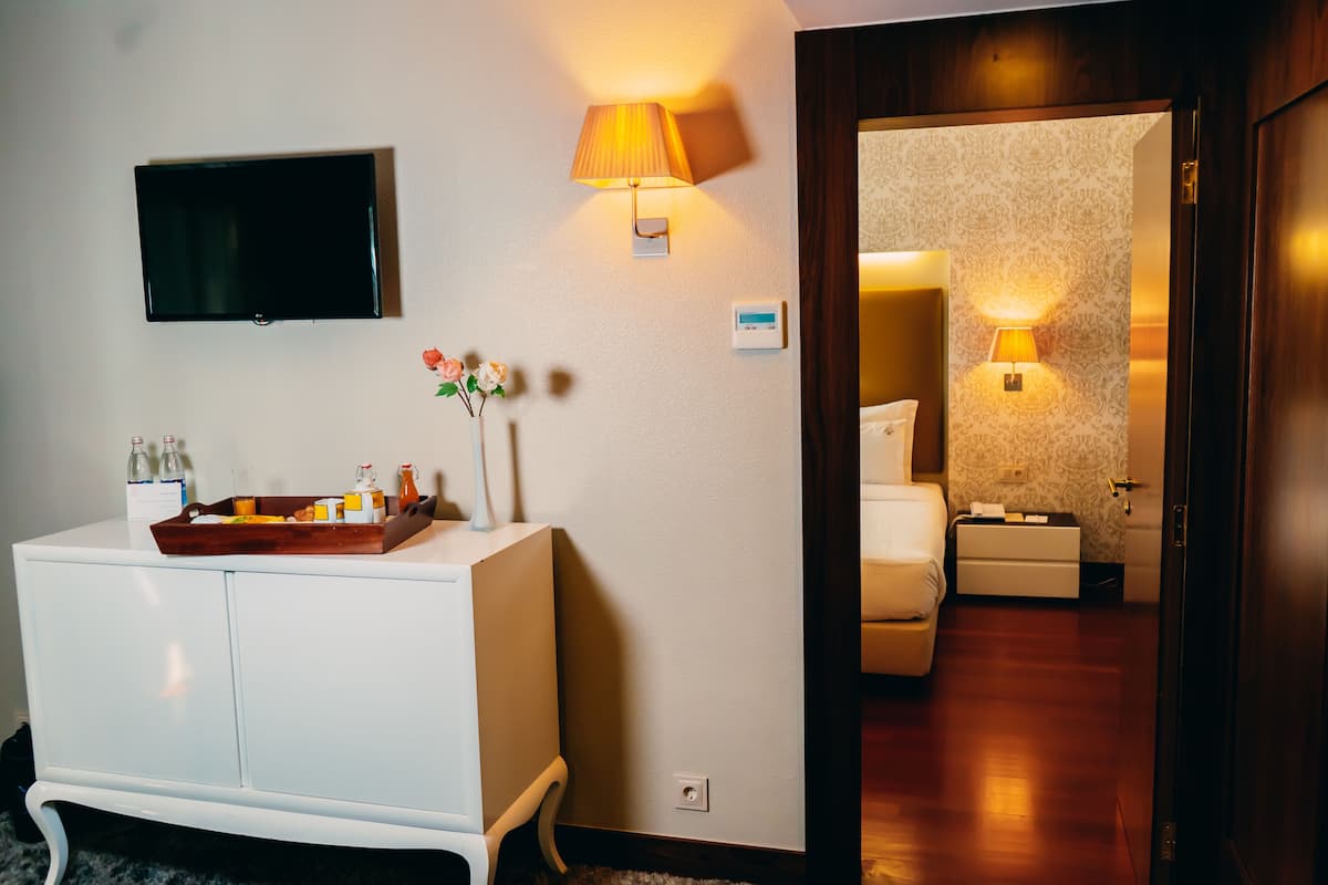 Une chambre d’hôtel équipée d’un téléviseur à écran plat fixé au mur, d’une lampe de chevet, d’une petite table ornée d’un vase de fleurs et d’une armoire en bois.