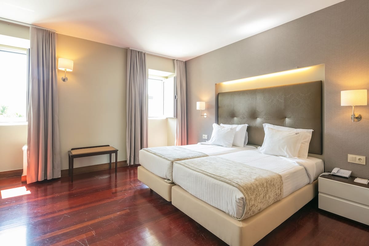 Une chambre d’hôtel avec deux lits, une table de chevet, une commode et une fenêtre avec des rideaux.
