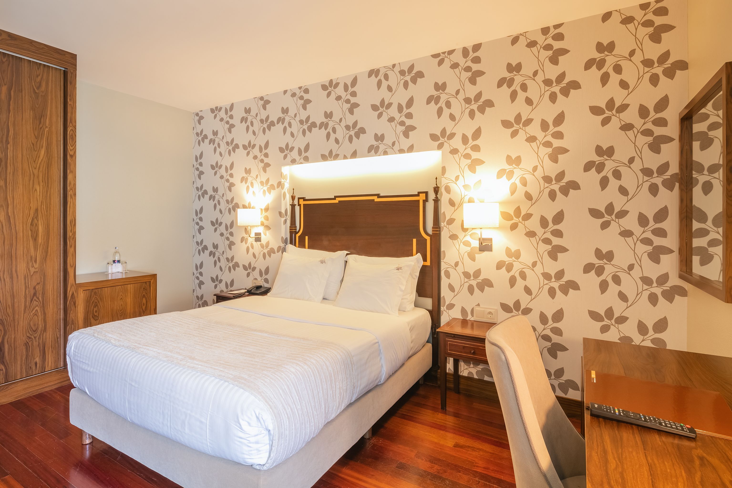 Ett hotellrum med en stor säng, sänglampor, ett nattduksbord i trä, ett skrivbord och en stol.