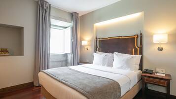 A hotel room with a large bed, two bedside lamps, a nightstand, and a window with curtains.