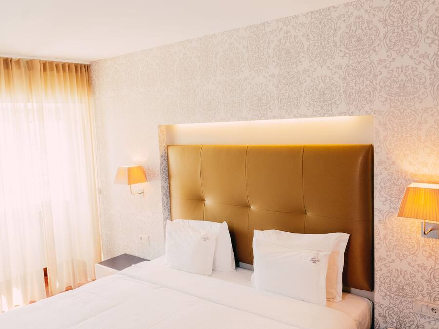 A hotel room with a large bed, two bedside lamps, and a patterned wallpaper.