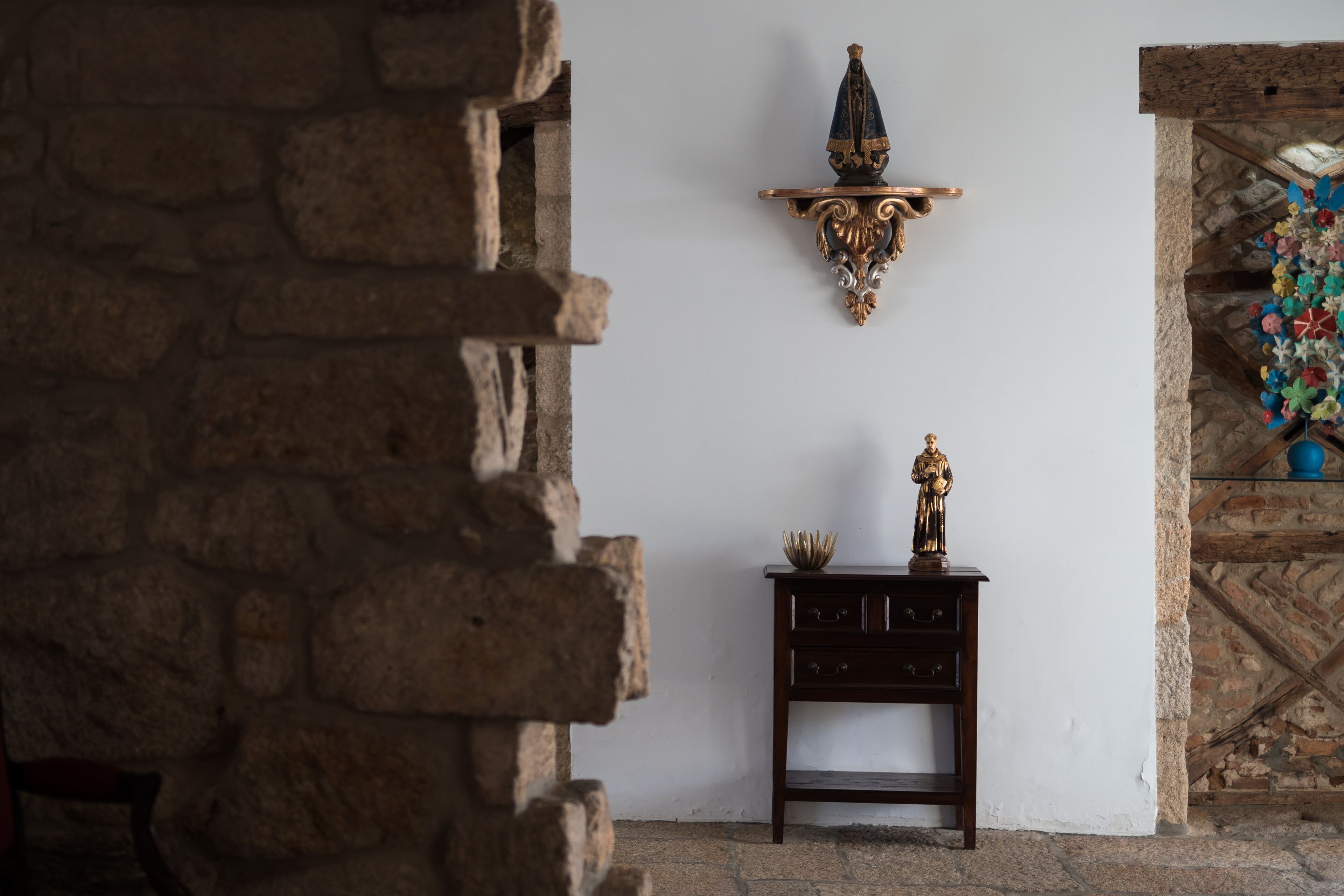 Un intérieur rustique avec un mur en pierre, un meuble en bois doté de tiroirs et un élément décoratif en métal accroché au mur.