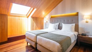 A hotel room with a vaulted ceiling, two beds, a bedside table with a lamp, and a window.