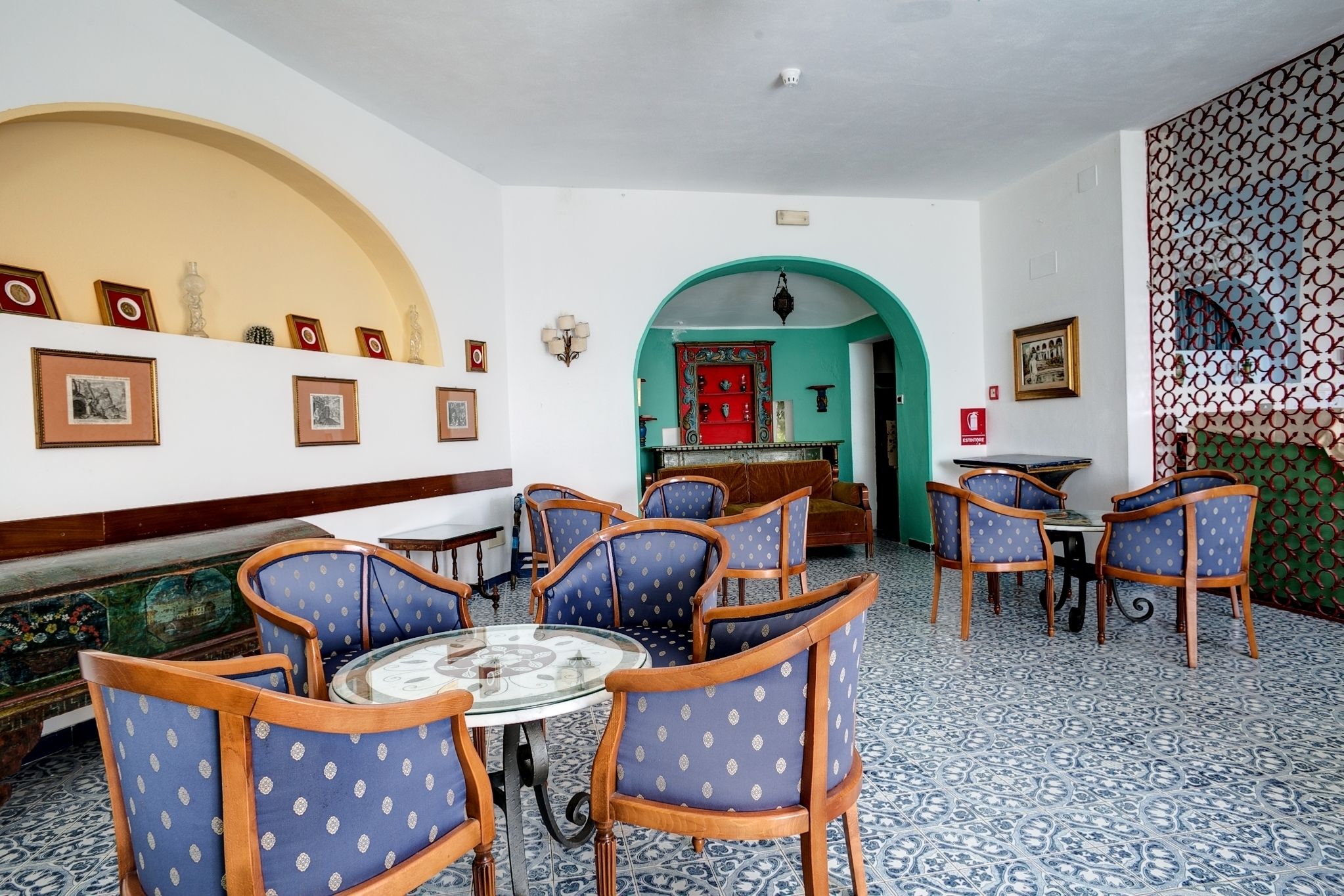 A room with a round table surrounded by blue chairs, a red door, and patterned floor tiles.