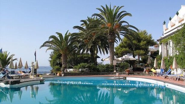 A pool with clear blue water, surrounded by palm trees and lounge chairs. - Arathena Rocks Hotel (Giardini Naxos)