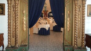 An ornate doorway with blue curtains leading to a dining area with tables set for a meal. - Arathena Rocks Hotel (Giardini Naxos)