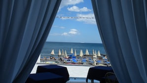 A view from a room with a window, overlooking a beach with lounge chairs and umbrellas. - Arathena Rocks Hotel (Giardini Naxos)