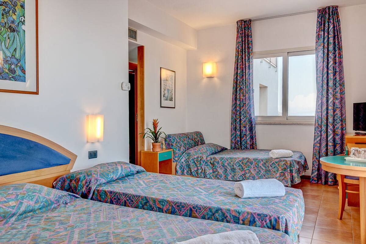 A hotel room with two beds, a small table, a TV, and a window with curtains.