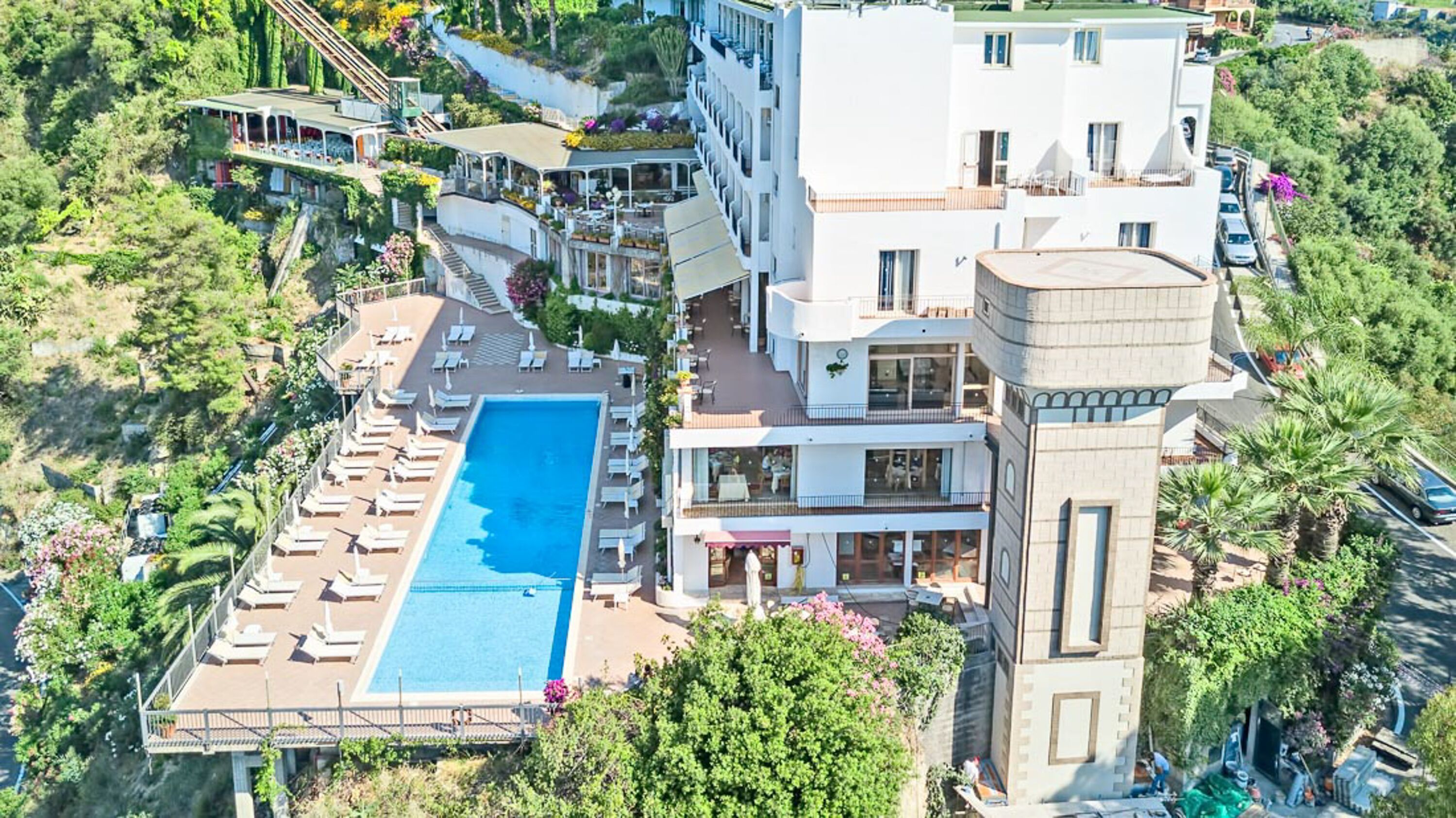 A multi-story hotel with a swimming pool, outdoor seating, and lush landscaping.