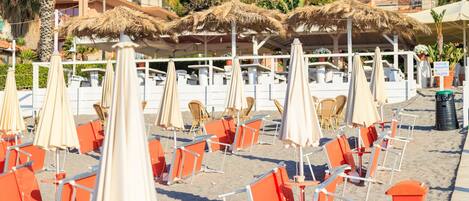 A beachside seating area with umbrellas and chairs, a sign indicating a toilet, and buildings in the background.