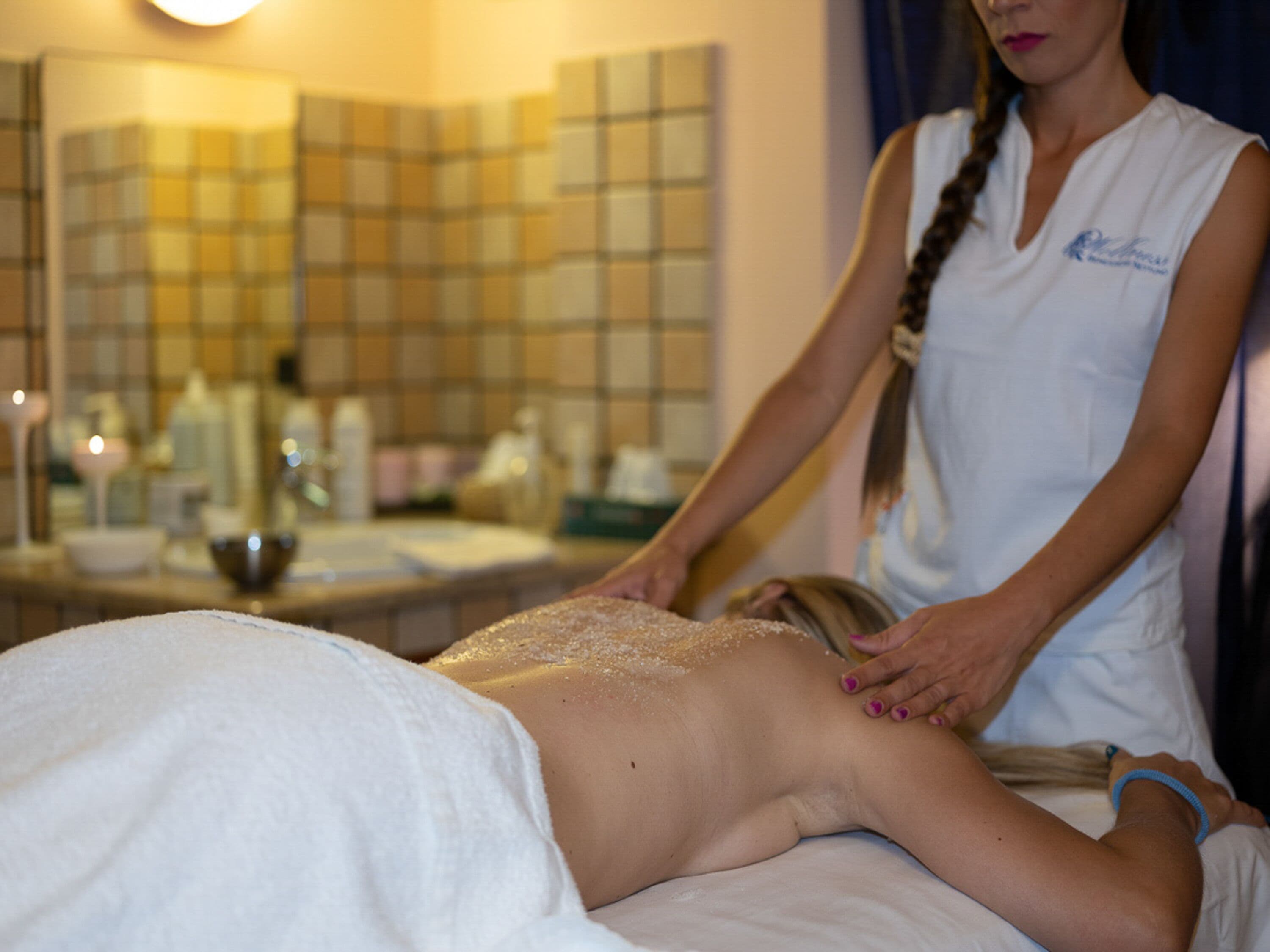 Eine Person erhält eine Massage in einem Raum mit rautenförmigem Muster an der Wand und einem Spiegel.