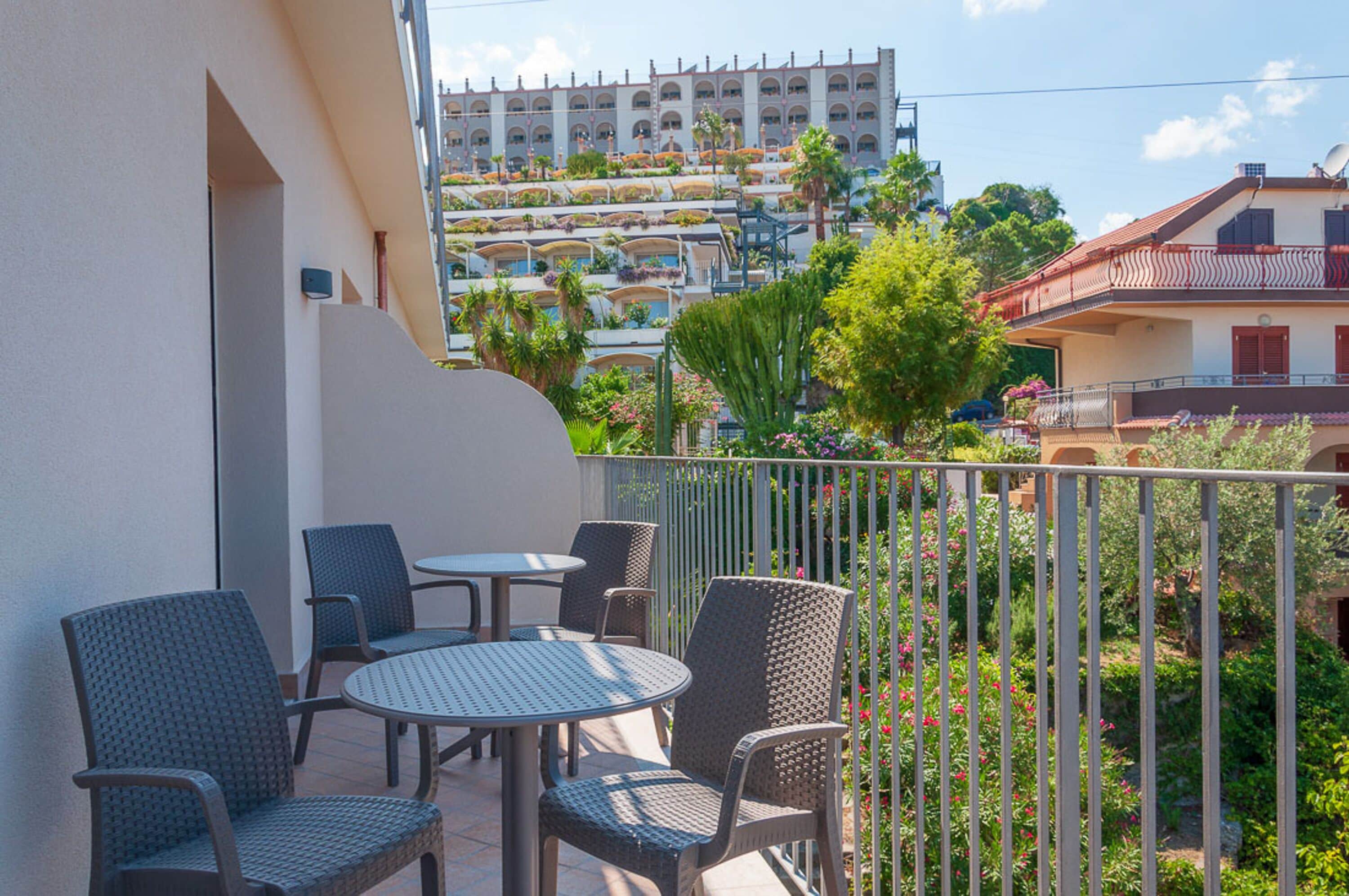 Un balcone con mobili in vimini e vista su un edificio alberghiero con numerosi balconi e vegetazione.