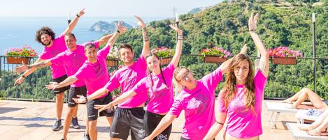 A group of people in pink shirts performing an exercise routine on a terrace with a scenic view of hills and the ocean.